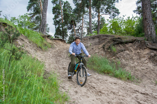 In the summer in a pine forest, a boy rides a bicycle down the mountain.