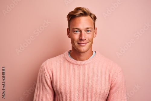 Headshot portrait photography of a beautiful boy in his 30s wearing a cozy sweater against a peachy pink background. With generative AI technology © Markus Schröder