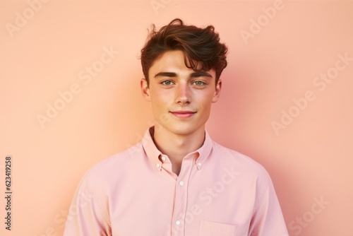 Headshot portrait photography of a glad boy in his 20s wearing a casual short-sleeve shirt against a peachy pink background. With generative AI technology