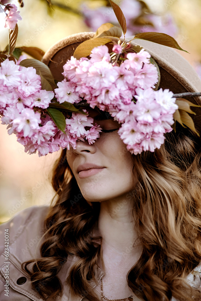 Naklejka premium Young girl with hat in a sakura garden