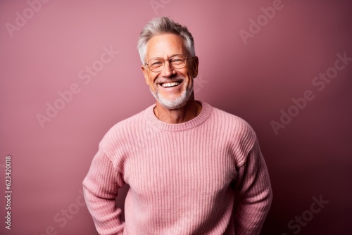 Environmental portrait photography of a happy mature man wearing a cozy sweater against a dusty rose background. With generative AI technology