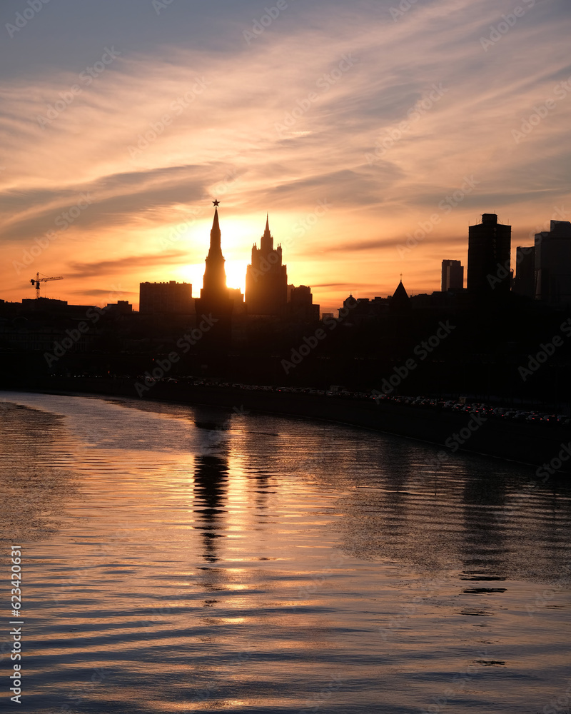 City landscape with Moscow river, embankment and silhouettes of buildings and Kremlin towers in crimson sunset