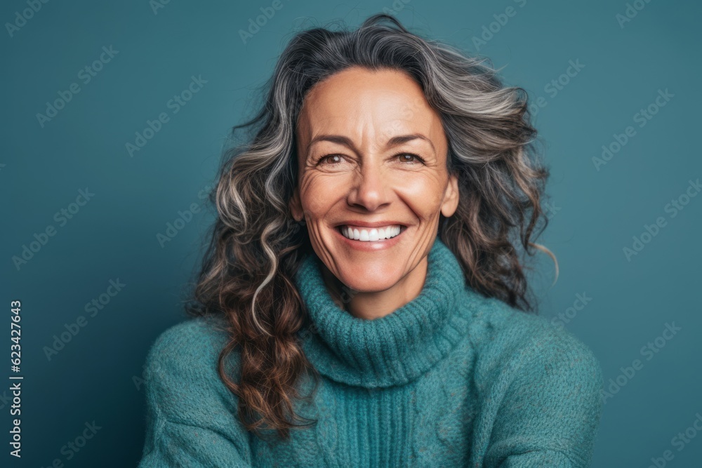 Fototapeta premium Close-up portrait photography of a happy mature woman wearing a cozy sweater against a teal blue background. With generative AI technology