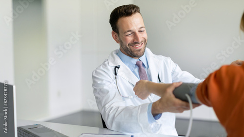 Cheerful male doctor measuring blood pressure to female patient while chatting with lady and smiling during medical examination  panorama copy space