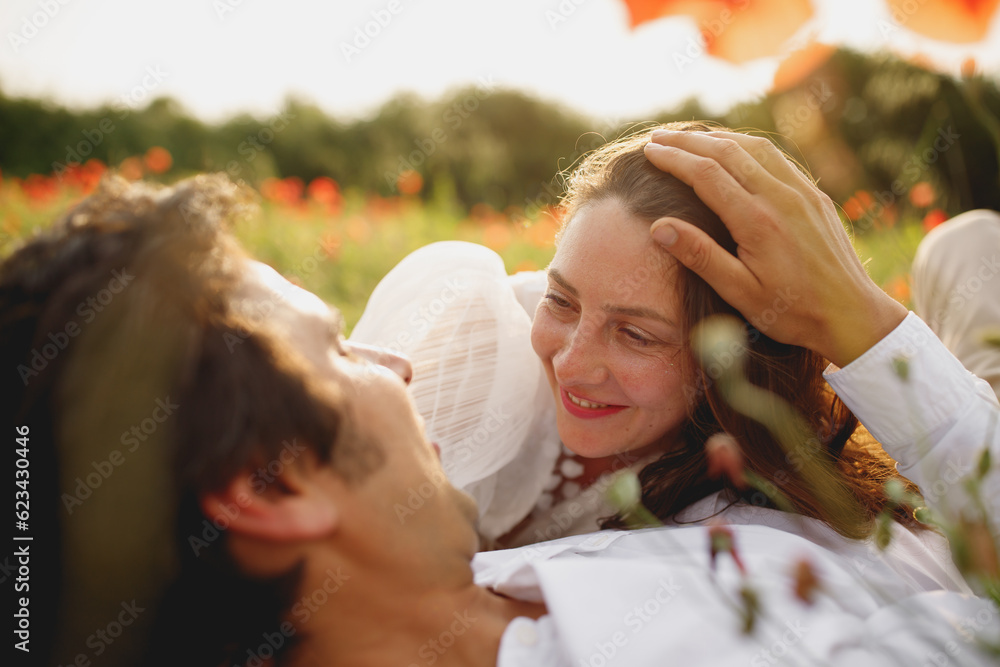 Obraz premium The close portrait of wedding couple laying at the poppies field laughing smiling