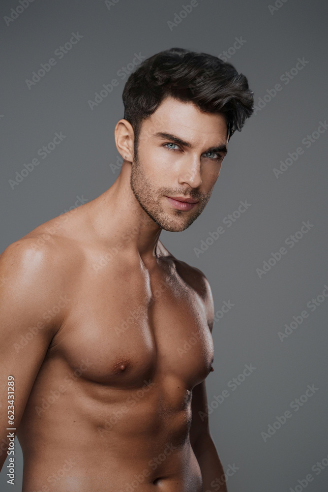 Charismatic close-up of a shirtless brunette model with a fit and toned physique against a modern gray backdrop Charismatic close-up of a shirtless brunette model with a fit and toned physique against a modern gray backdrop