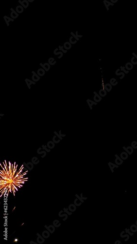 Slow-motion filming shining pyrotechnic display with colorful lights in the night, the flickering golden lights of fireworks in the black sky, vertical video. 