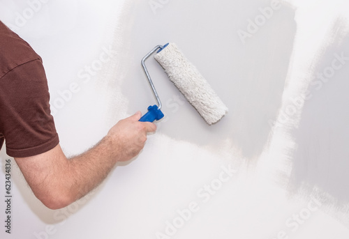 The male hand of the painter, holds a paint roller on the background of the wall.