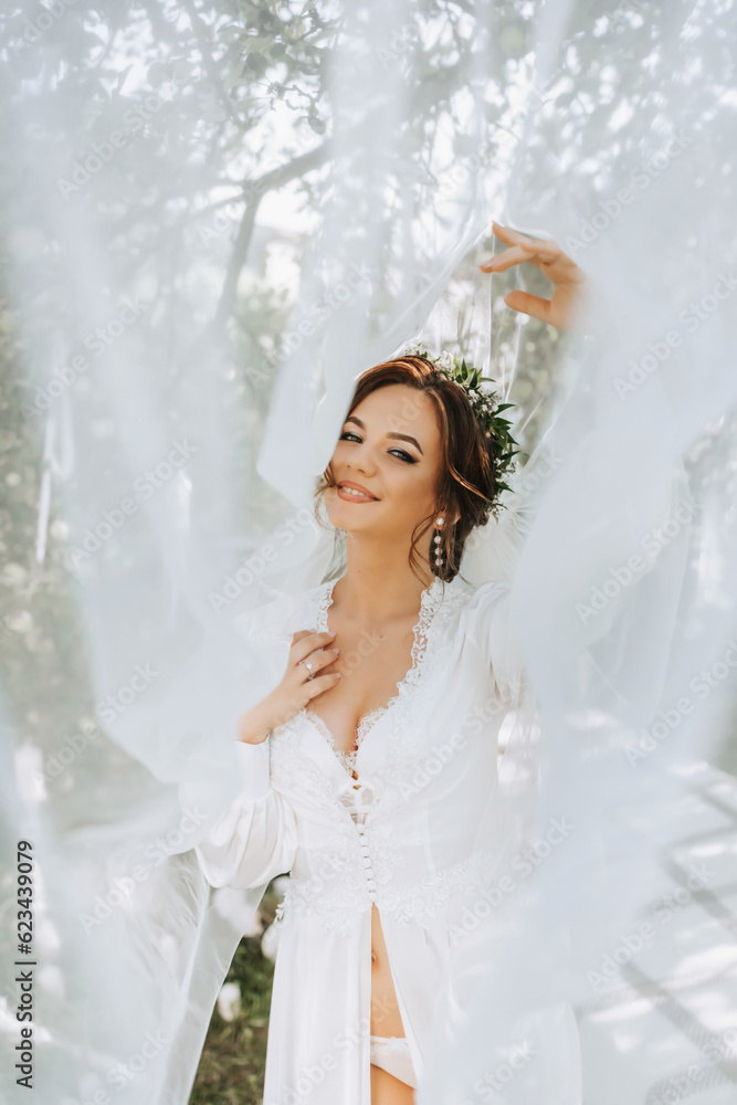 portrait of a dreamy bride standing by a bed in a garden under a veil. The bride is dressed in a white robe and a tiara of fresh flowers on her head portrait of a dreamy bride standing by a bed in a garden under a veil. The bride is dressed in a white robe and a tiara of fresh flowers on her head