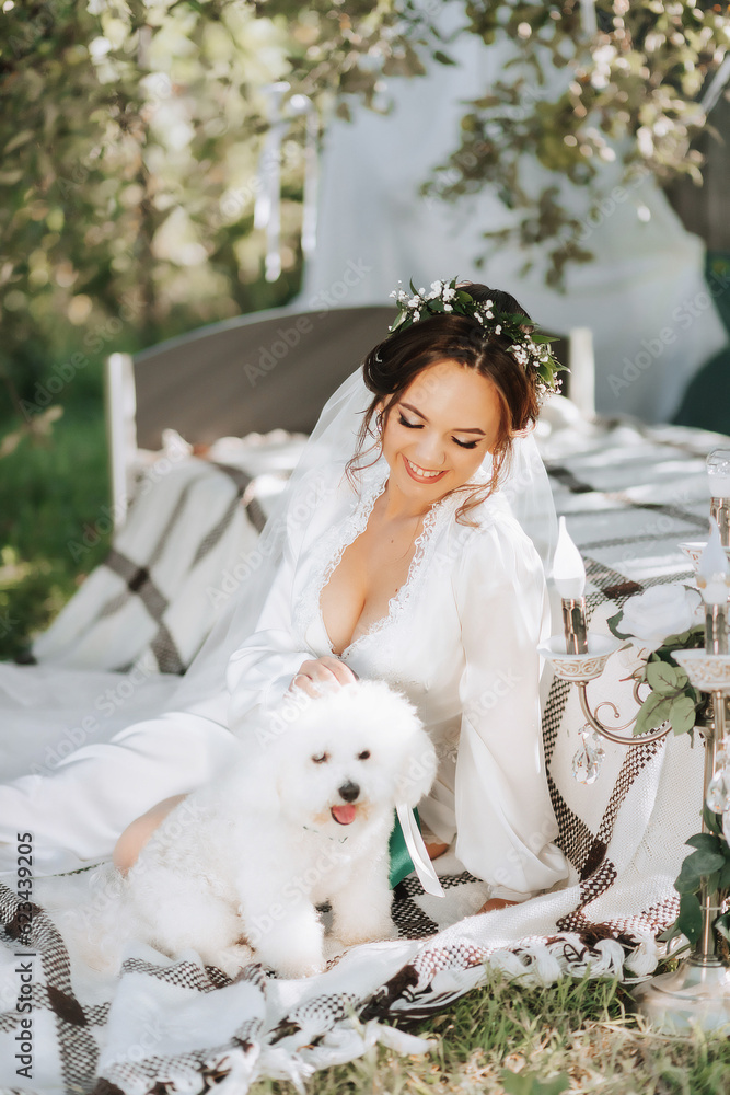 young elegant bride in a white dress with a tiara of fresh flowers on her head posing in the garden with her poodle dog young elegant bride in a white dress with a tiara of fresh flowers on her head posing in the garden with her poodle dog