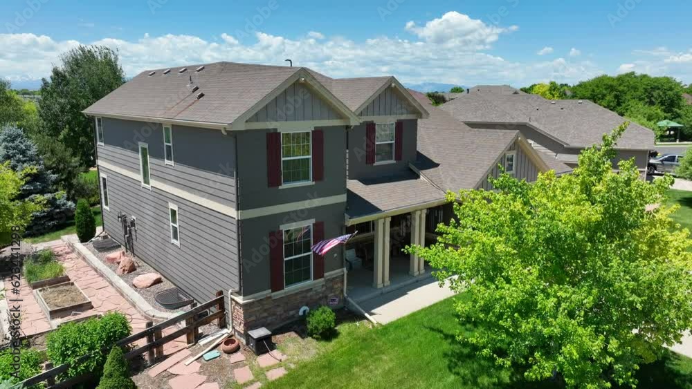 American flag waving on beautiful family house in Colorado. Aerial rising shot reveals sprawling neighborhood in summer with Rocky Mountains in distance. American flag waving on beautiful family house in Colorado. Aerial rising shot reveals sprawling neighborhood in summer with Rocky Mountains in distance.