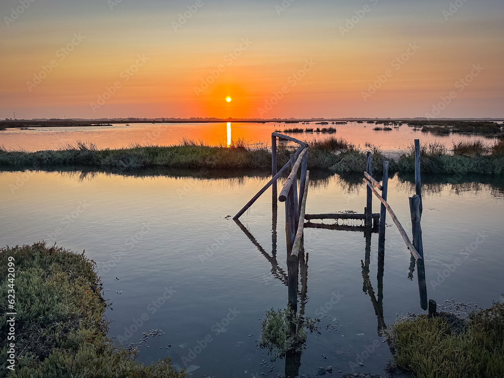 Old wooden pier at the Ria de Aveiro in Portugal, with calm water at sunset. Murtosa, Portugal.