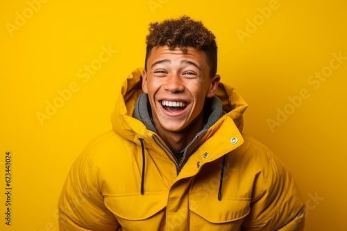 Medium shot portrait photography of a happy boy in his 30s wearing a warm parka against a yellow background. With generative AI technology