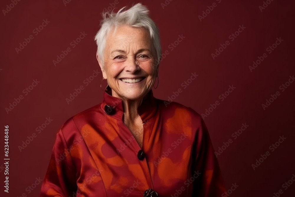 Medium shot portrait photography of a grinning old woman wearing a trendy jumpsuit against a burgundy red background. With generative AI technology