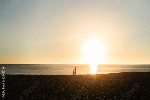 SIlueta de surfista al atardecer en la playa esperando frente al mar con tabla de surf