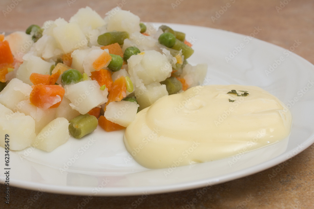 A close up view of a creamy and smooth mayonnaise sauce, served with a plate of Russian salad, a mix of potatoes, carrots, peas, tuna, and mayonnaise. A sprinkle of parsley adds some color and freshne A close up view of a creamy and smooth mayonnaise sauce, served with a plate of Russian salad, a mix of potatoes, carrots, peas, tuna, and mayonnaise. A sprinkle of parsley adds some color and freshne