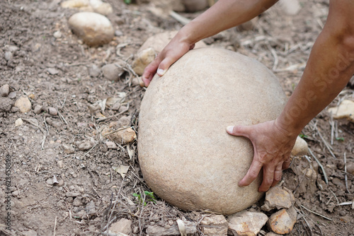 Close up hand is lifting big stone from ground. Concept, heavy. Hard working. Strong body to lift or move heavy rock. 