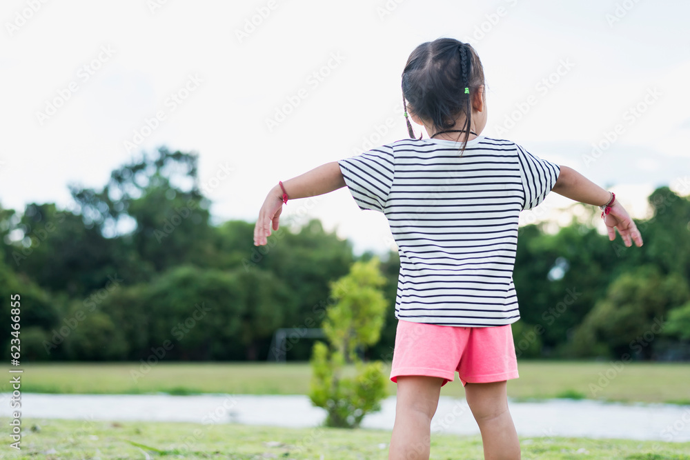 Happy Asian child in park standing with arms outstretched Young girl relaxing outdoors. Freedom concept.