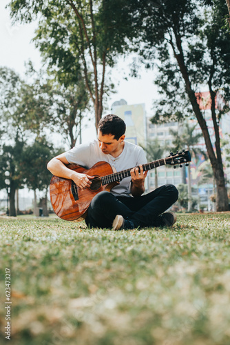 Portrait of young man playing acoustic guitar sitting on the lawn of a park. Concept of people and hobbies.