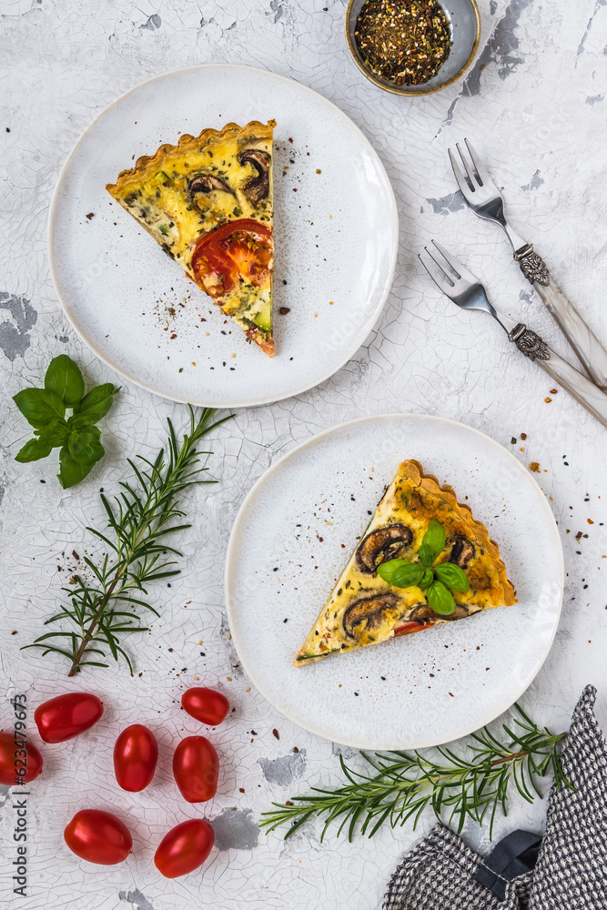 Two pieces of homemade vegetable tart with mushrooms, tomatoes and zucchini on white background, decorated with herbs, top view Two pieces of homemade vegetable tart with mushrooms, tomatoes and zucchini on white background, decorated with herbs, top view