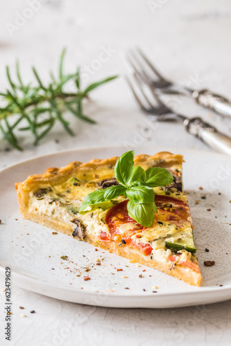 Piece of vegetable tart with mushrooms, tomatoes and zucchini on white background, vertical