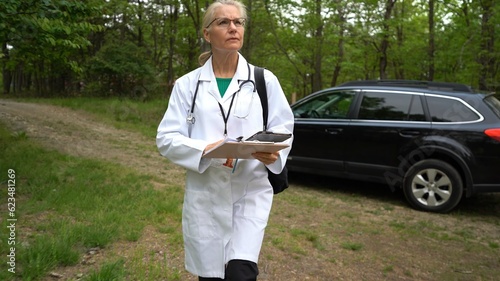 Mature woman nurse or doctor gets out of car, walks to door for a home visit in a rural area.