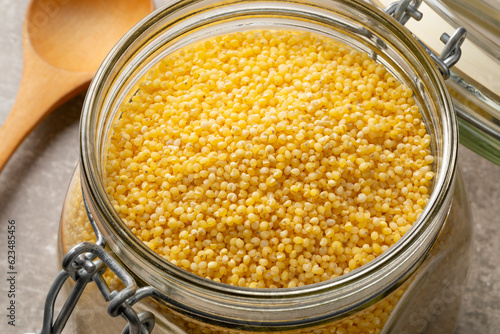 Glass jar with raw dry yellow millet  close up seen from above 