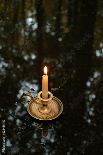 burning candle in candlestick in puddle close up, abstract dark natural background. rainy weather, summer or autumn day. melancholy atmosphere image. template for design