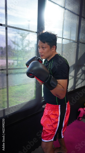 Thai boxing man in gym with sandbag. Athlete man in fitness with glove train in punching and kicking. Martial art exercise for strength. © soultkd