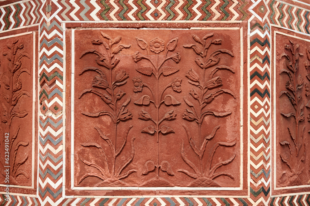 Decorative flowers on red sandstone wall of Taj Mahal, beautiful ancient wall decorations depicting flowers plants, old red sand stone handmade ornament decoration in Taj Mahal landmark building Decorative flowers on red sandstone wall of Taj Mahal, beautiful ancient wall decorations depicting flowers plants, old red sand stone handmade ornament decoration in Taj Mahal landmark building