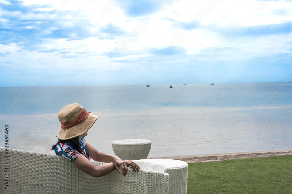 Relaxing woman wear beach hat sitting on beach chair looking at the sea on Holiday and summer Vacation