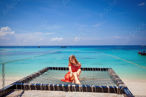 Woman in red dress enjoys leisure time in a hammock on a tropical beach. Concept of a serene summer getaway and ultimate tranquility.