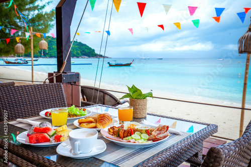 Table with breakfast on the beach. Summer vacation at a luxurious resort with a beautiful view of the ocean. Fresh food and refreshing juice. Concept of relaxation and paradise.