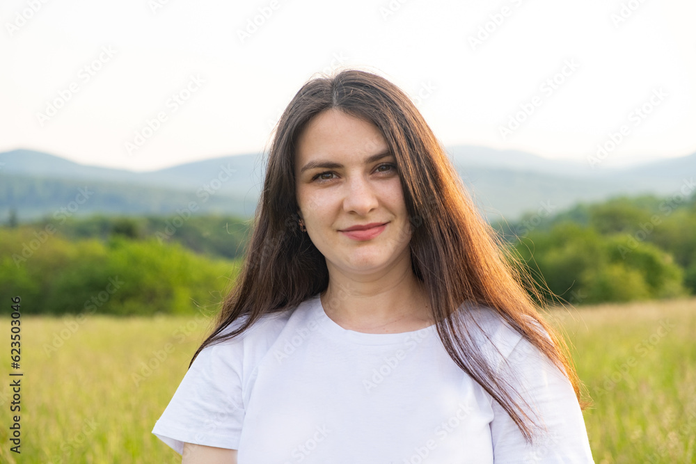 Portrait of a 30-year-old European woman smiling while looking at the camera while walking in nature in a field.
