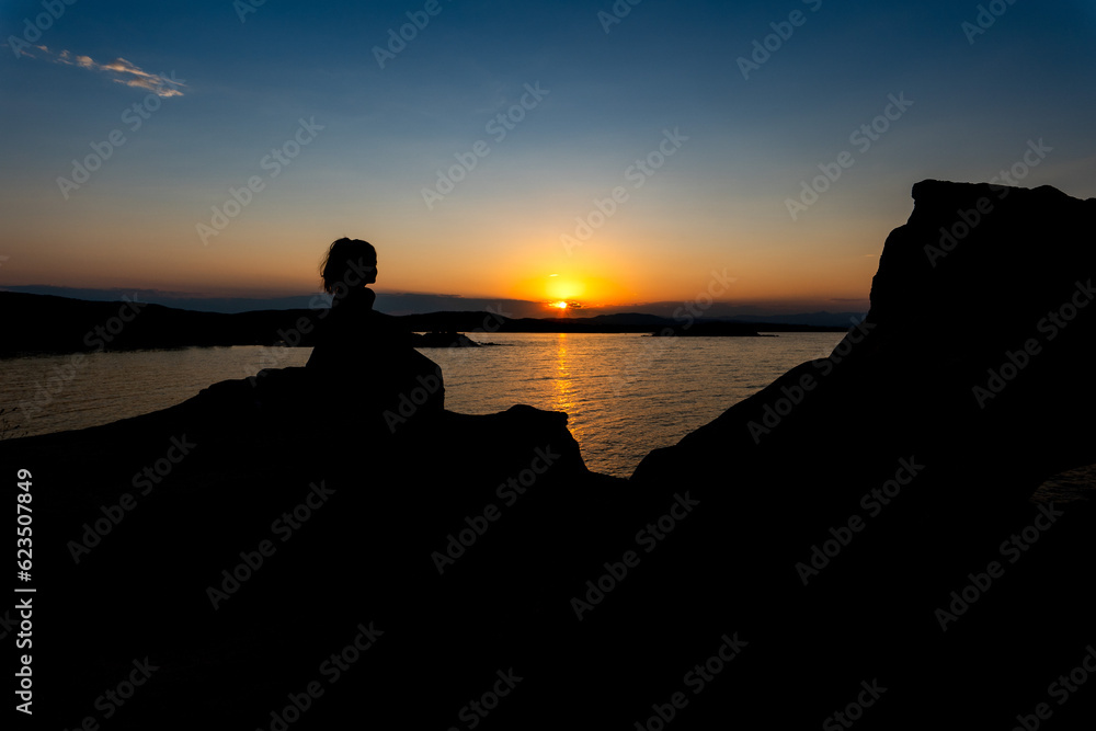 silhouette of a person sitting on a rock at sunset