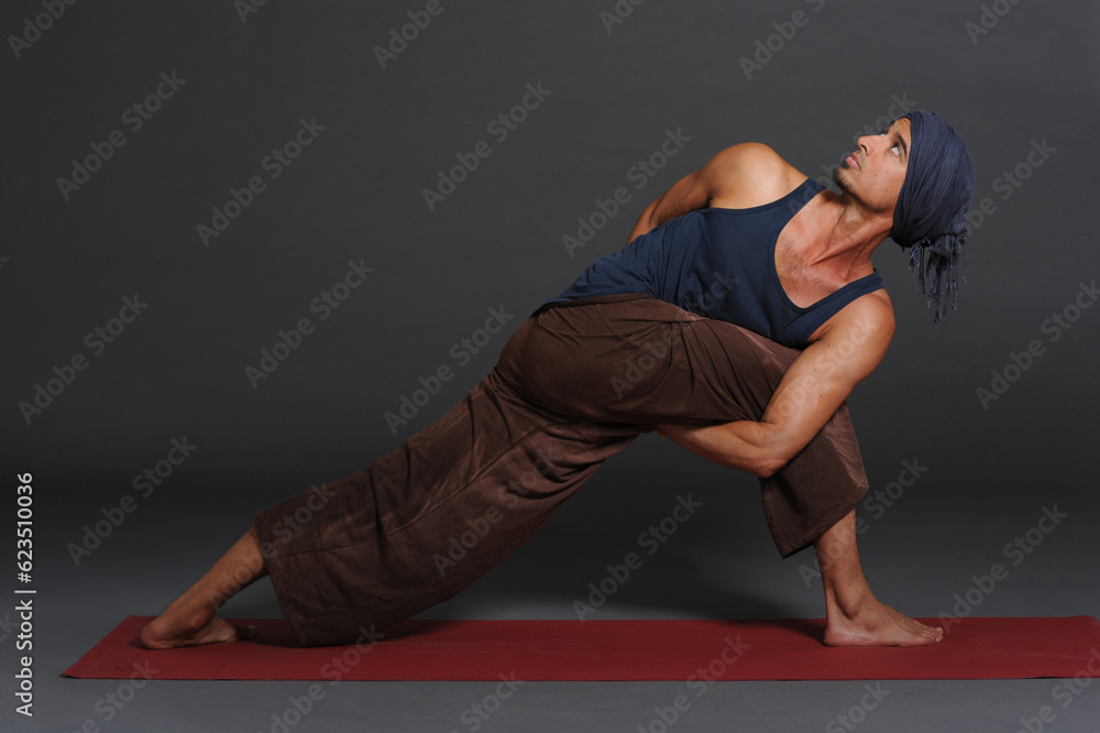 Man doing yoga in photo studio on isolated grey background.
