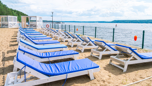 Deck chairs with throw mattresses for relaxing on the beach. Relaxing on the beach by the sea. Summer tan by the water. A relaxation area with sun loungers on the sandy beach for sunbathing.