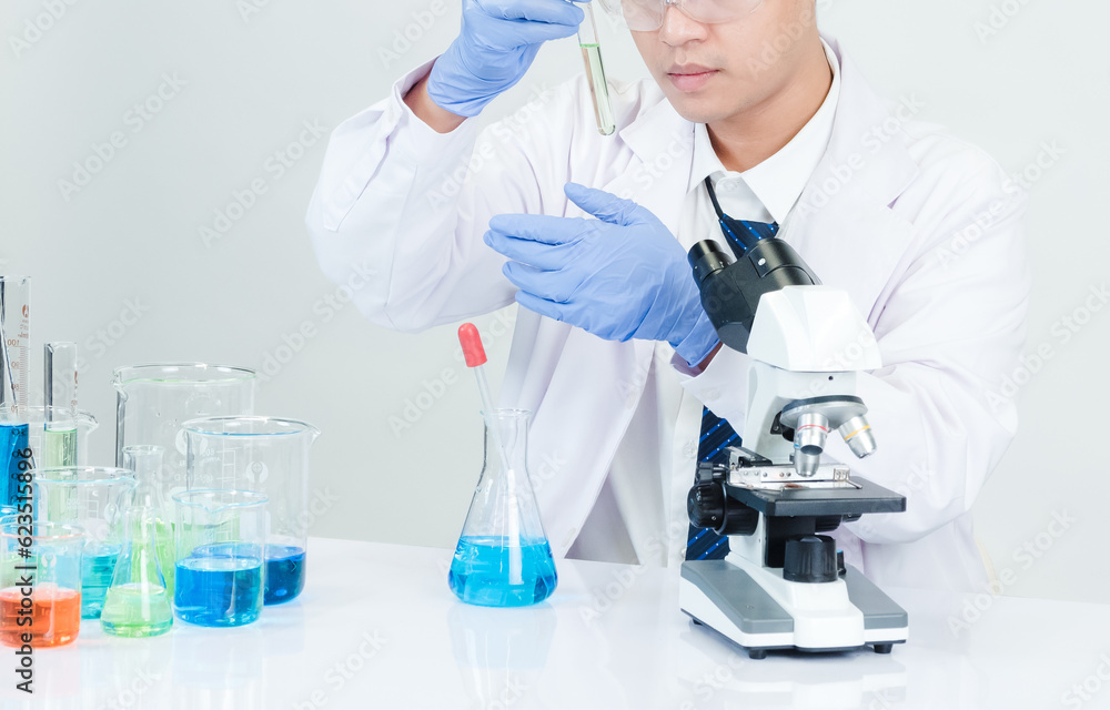 Man asian student scientist Wearing a doctor's gown in the lab looking at the chemist. caused by mixing reagents in scientific research laboratories with test tubes and microscope on the table Man asian student scientist Wearing a doctor's gown in the lab looking at the chemist. caused by mixing reagents in scientific research laboratories with test tubes and microscope on the table