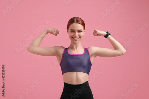 Fototapeta Naklejka Na Ścianę i Meble -  Young woman in sportswear showing muscles on pink background