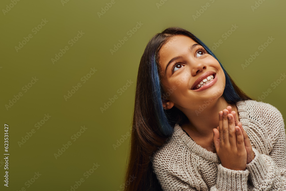 Portrait of smiling brunette preteen girl with dyed hair wearing knitted sweater while doing praying hands gesture and standing isolated on green, fashion-forward preteen with sense of style Portrait of smiling brunette preteen girl with dyed hair wearing knitted sweater while doing praying hands gesture and standing isolated on green, fashion-forward preteen with sense of style