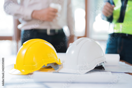 yellow and white helmet image For use on the table, there is a blueprint. Behind it, there is an engineer or architect talking about the design industry. Wear vests and uniforms. in the workplace