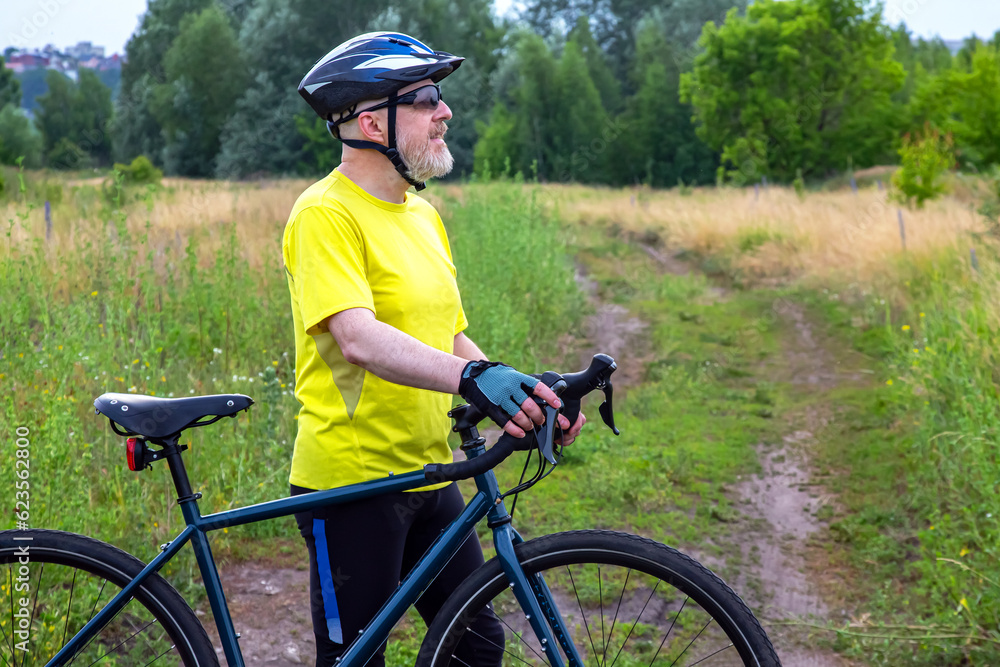 bearded man cyclist in yellow clothes is resting on a bicycle on the road in nature. sports, hobbies and entertainment for health bearded man cyclist in yellow clothes is resting on a bicycle on the road in nature. sports, hobbies and entertainment for health