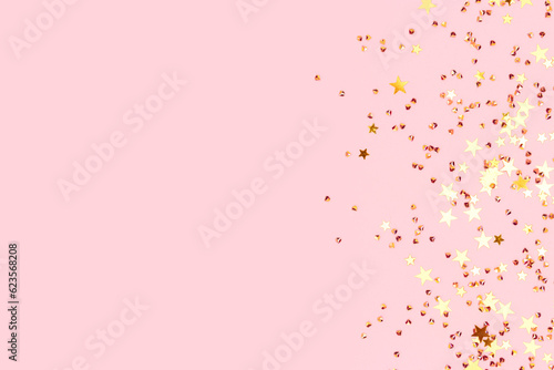 Glowing gold colored stars and crystals confetti on a pink background. Festive concept with place for text. Selective focus.