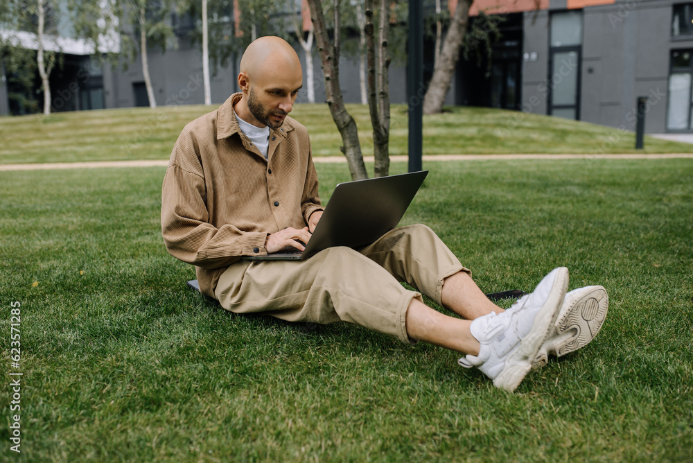 Young entrepreneur student freelance tutor using laptop for remote remote work, checking email, e-banking online, sitting on green grass lawn Young entrepreneur student freelance tutor using laptop for remote remote work, checking email, e-banking online, sitting on green grass lawn