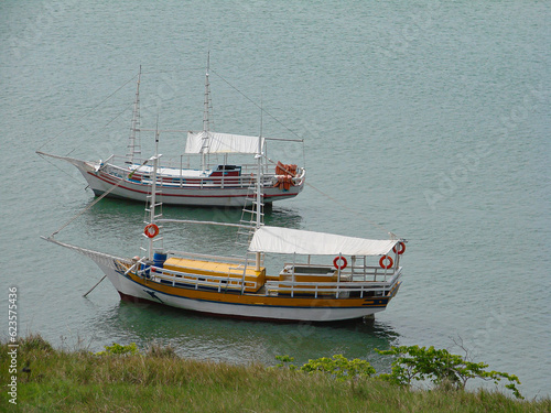 Two boats, white, with red details, another white, with yellow and orange details, with buoys on board, sail through the waters of Natal, on the coast of Brazil.