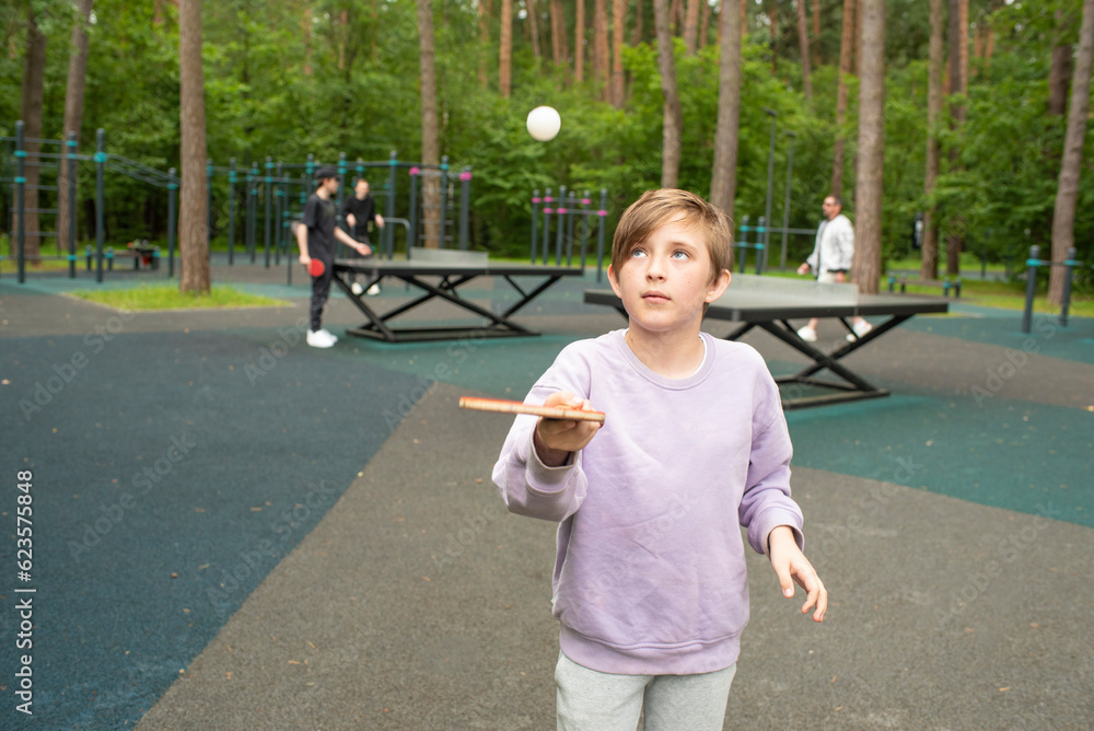 A 10yearold boy tosses and hits a table tennis ball on a sports field