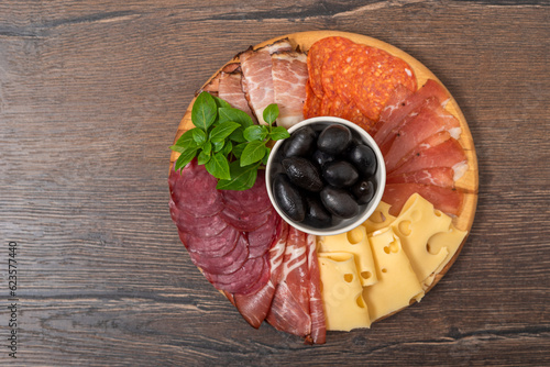 Meat plate with cuts of prosciutto, salami, bacon, cheese and olives on a wooden cutting board.
