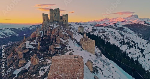 Aerial view of the Rocca di Calascio with snow and illuminated by the light of the sunset, behind the chain of the Gran Sasso and the Corno grande. Gran Sasso and Monti della Laga National Park, Abruz photo