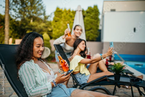 Women relax on the lounge chairs, soaking up the sun, using a phone, and enjoying the warm weather. Focus on an Asian woman