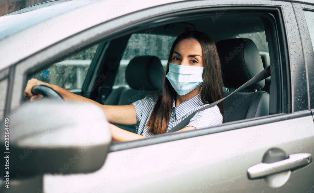 Beautiful young woman in safety mask sitting in a car, protective mask against coronavirus, driver on a city during a coronavirus outbreak. Business trips during pandemic